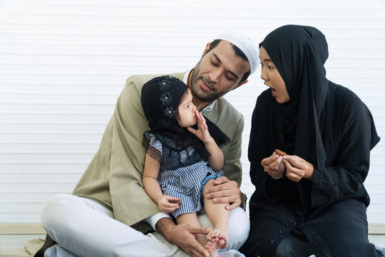 Muslim family with playful little daughter and mother showing funny surprised face while eating dates isolated on white background with copy space.