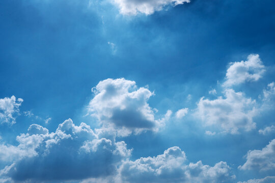 Beautiful bright blue sky with fluffy white cumulus clouds and sunlight shining through. Perfect natural weather background with ample copy space for text or design layout.