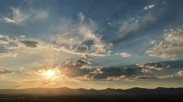 A 4k drone timelapse of dozens of light rays moving through a brilliant gold and blue sky, emphasizing dramatic weather patterns over a dark silhouetted Southwest mountain range.