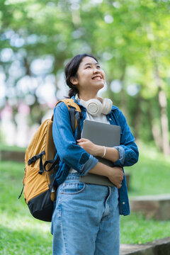 Happy student standing outdoors holding laptop looking up