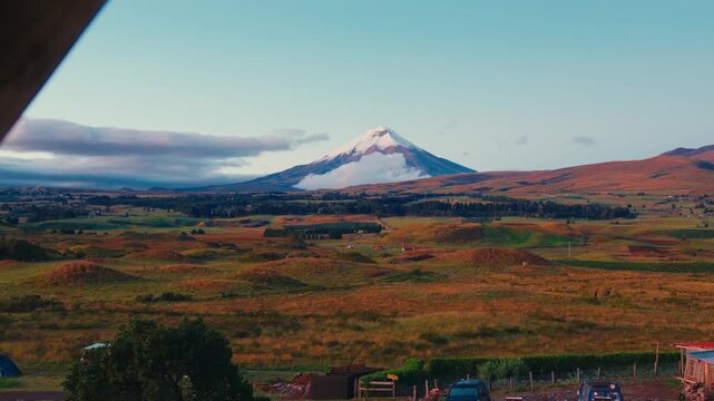 Cotopaxi volcano rises above clouds over rolling hills and farmland in Ecuador