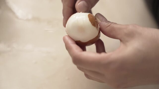 Close-up of caucasian hands peeling a brown boiled egg with difficulty