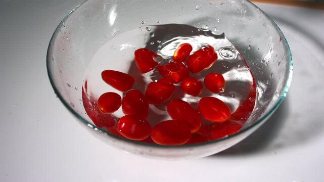 Dropping cherry tomatoes in bowl of water for washing medium 4k slow motion shot selective focus