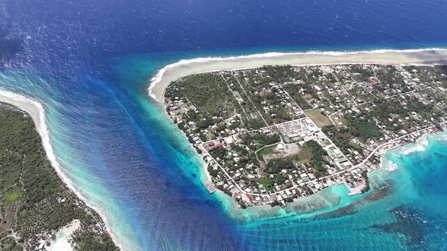 Aerial view pushing forward over Avatoru Pass, capturing a vibrant marine channel flowing between deep blue ocean waves and a shallow turquoise island lagoon