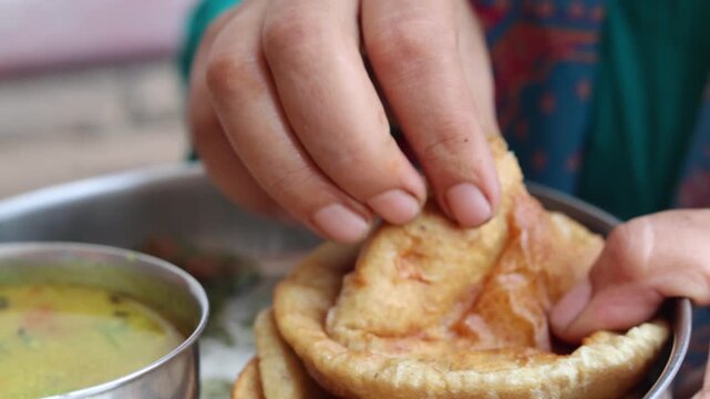 Close-up of an Indian woman eating puri with curry by hand, showing traditional Indian food, homemade cuisine and everyday eating habits.