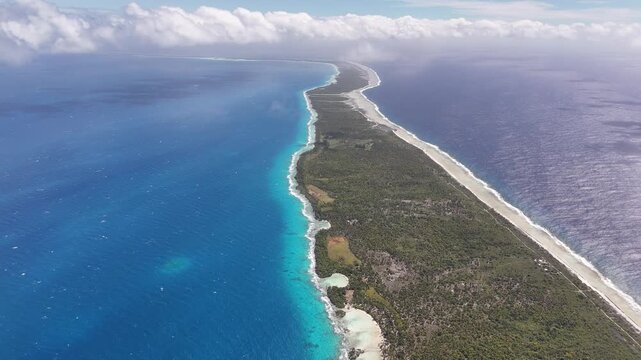 High-altitude drone rising shot establishing the narrow coral land strip of Rangiroa Atoll, flanked by a vibrant turquoise inner lagoon and the deep blue South Pacific Ocean