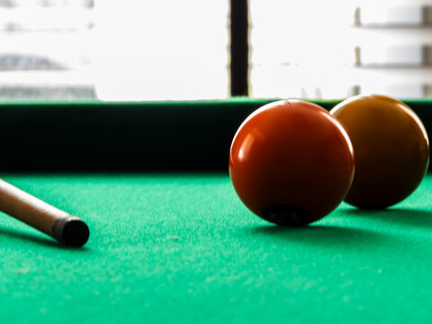 Close-up of billiard balls and pool cue on green felt table. A selective focus shot of colorful numbered balls scattered on a green snooker table with a wooden pool 