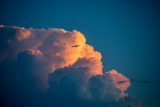 Silhouetted airplane navigating past a colossal cumulus cloud illuminated by sunset light. For overcoming business obstacles, navigating uncertainty, corporate resilience, ambitious goals