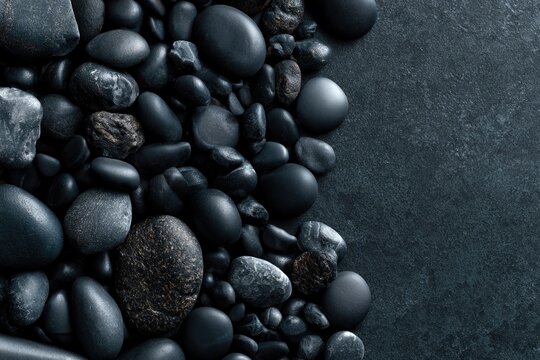 Smooth and textured black stones arranged on a dark surface, creating a sleek and natural minimalist composition.