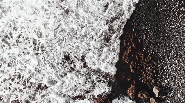 Cinematic high-angle view of waves crashing against the rocks.