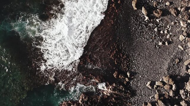 Cinematic high-angle view of waves crashing against the rocks.