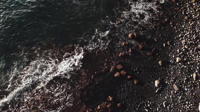 Cinematic high-angle view of waves crashing against the rocks.