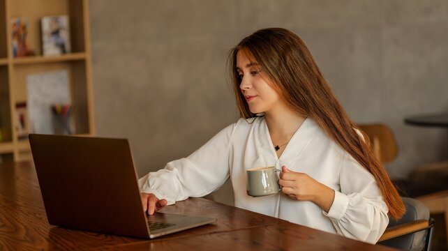 Young woman working on laptop while holding a coffee mug in a cafe