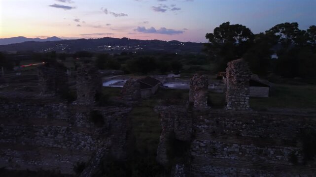 Cinematic drone camera orbiting left while flying right over the historic ruins of Nikopolis during a beautiful golden hour sunset.