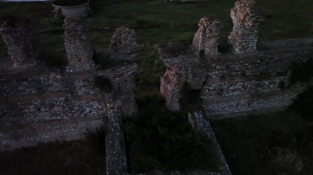Cinematic 360-degree rotational drone camera movement orbiting the historic ruins and brick walls of ancient Nikopolis during low light twilight.