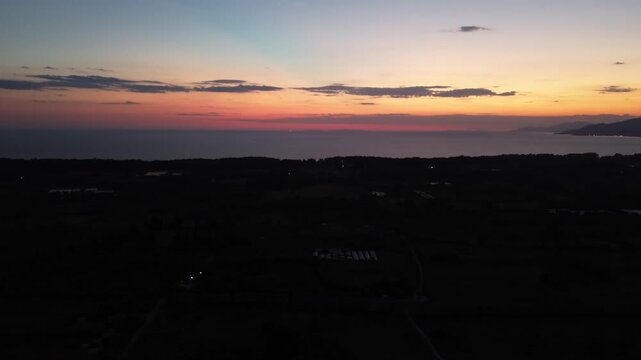 Cinematic drone shot capturing the vibrant orange and pink twilight sky over the calm waters of the Ionian Sea at dusk.