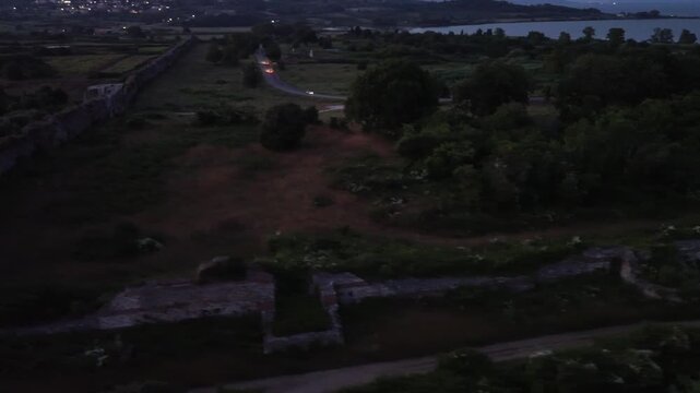 Panoramic high-altitude drone shot capturing the linear fortification layout of ancient Nikopolis brick walls surrounded by green fields at dusk.