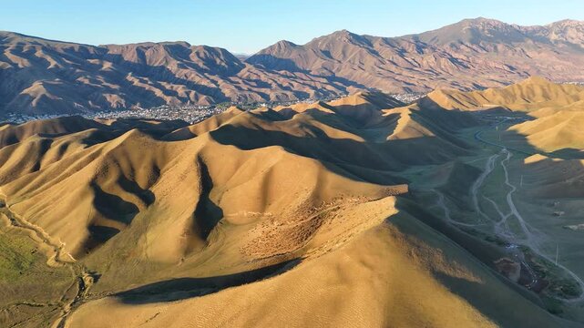 An aerial view of a landscape typical of Kyrgyzstan. The contours of the hills and pastures around the town of Naryn, with the Tian Shan in the background. A summer holiday and the adventure of travel