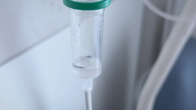 Extreme close-up of the bottom of the drip chamber on an IV set-up in hospital as clear fluid drips down.