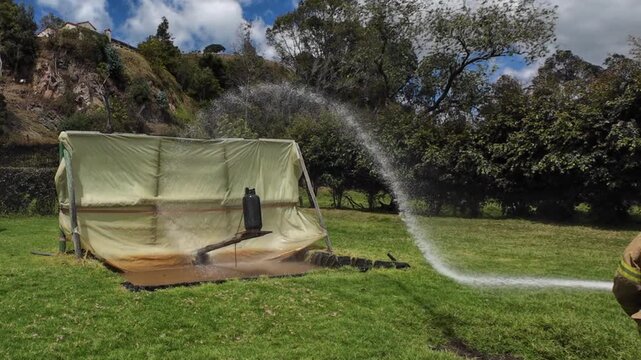 Firefighter spraying water from a fire hose during a training exercise to control a gas cylinder