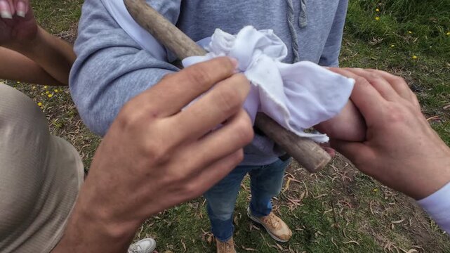 Person providing first aid by applying an improvised splint to an injured arm after an accident
