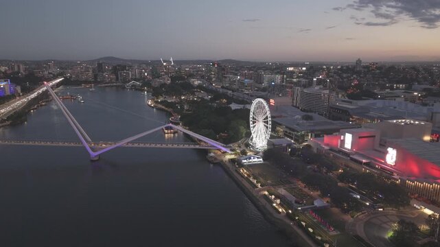 A night aerial view shows the purple lit Neville BonnerBridge beside the illuminated Wheel of Brisbane.