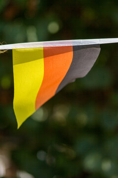 Small Triangular German Flag Bunting Garland Against Blurred Green Foliage, Close-Up