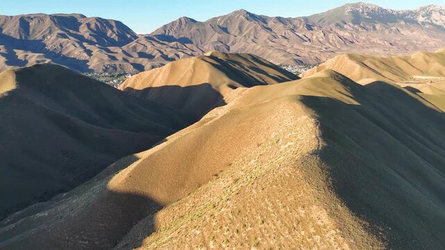 An aerial view of a landscape typical of Kyrgyzstan. The contours of the hills and pastures around the town of Naryn, with the Tian Shan in the background. A summer holiday and the adventure of travel