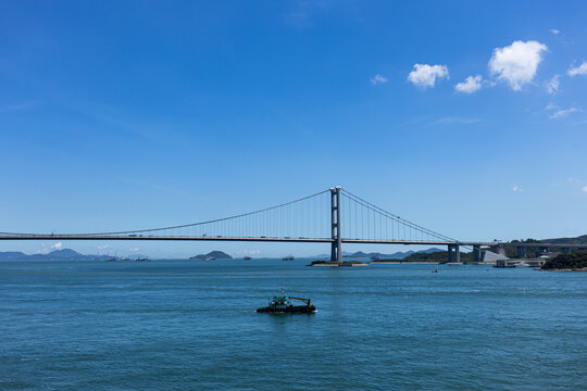 View of a bridge connecting two land areas with fishing boats in the water under a clear blue sky