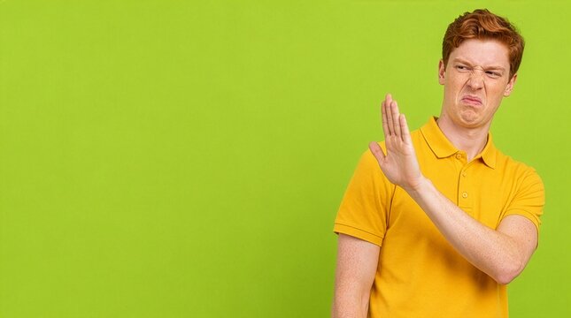 Disgusted young redhead man making stop gesture on green background