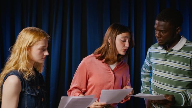 Diverse group of young adult acting students surprising classmate with birthday cake on stage during rehearsal, camera zooming out. Ideal for drama school marketing and youth friendship campaigns