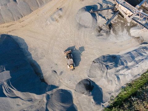 Wheel Loader in the Middle of an Aggregate Stockpiling Area. Heavy Construction Machinery Surrounded by Rock, Sand, and Processed Materials at an Industrial Mining Site view from above.