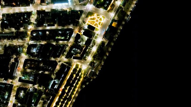 Saratov, Russia. Cosmonauts Embankment, aerial night view over the Volga riverfront with illuminated terraces and the Saratov Bridge glowing against the dark water. Drone footage, HEAD OVER SHOT