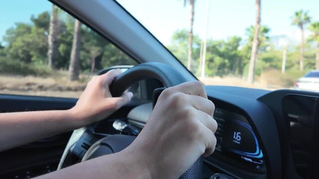 Close view of driver hands on the steering wheel while driving on a sunny road, slow motion