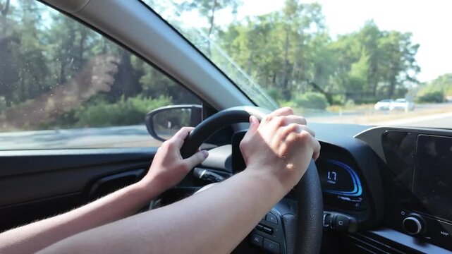 Driver holding the steering wheel while traveling on a sunny road, close up view