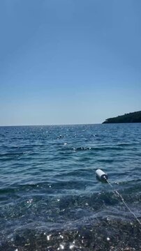 Floating buoys in clear blue sea near a sunny coastline, vertical video