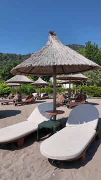Empty sun loungers under straw beach umbrellas at a sunny mountain resort, vertical video