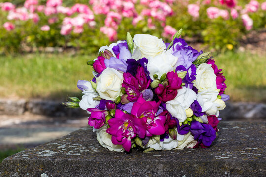 Colorful wedding bouquet resting on stone with roses in background