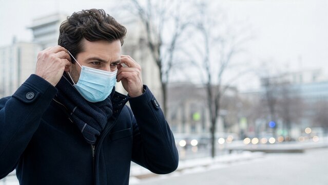 Man putting on a protective face mask outdoors in winter city during cold and flu season, illness prevention and public health protection concept