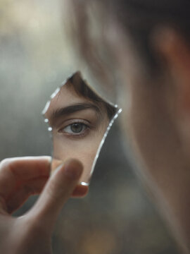 A captivating close-up photograph of a human eye viewed through fractured glass. The eye appears to be looking towards the viewer, with the eyelids slightly raised.