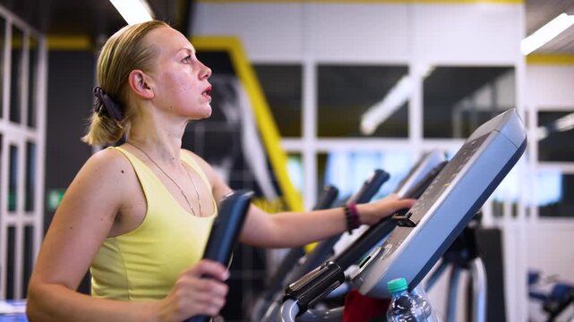 Close-up of a middle-aged woman engaged in a cardio workout on a step machine, showcasing her dedication to fitness and the importance of maintaining a healthy lifestyle. Slow motion footage.