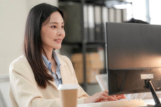 She laughs quietly at something on the monitor and keeps working, in a modern Thai design studio, creative colleagues reviewing green building ideas and eco friendly materials.