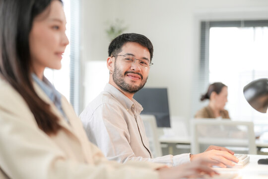 He leans forward and starts clicking through something on screen, at a sustainable design studio in Bangkok, a modern Asian creative team working on green architecture ideas together.