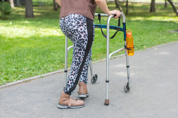 Obraz premium A young woman with cerebral palsy walks in a park with a walker.