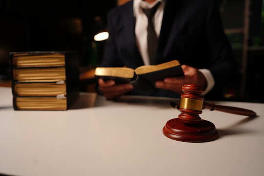 Lawyer holding open law book sitting behind wooden judge gavel and stack of books