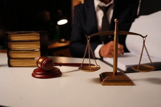 Lawyer holding open law book sitting behind wooden judge gavel and stack of books
