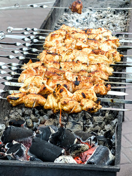 Grilled chicken pieces sizzle over glowing charcoal coals