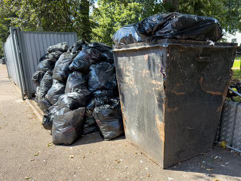 Black garbage bags pile beside a dumpster