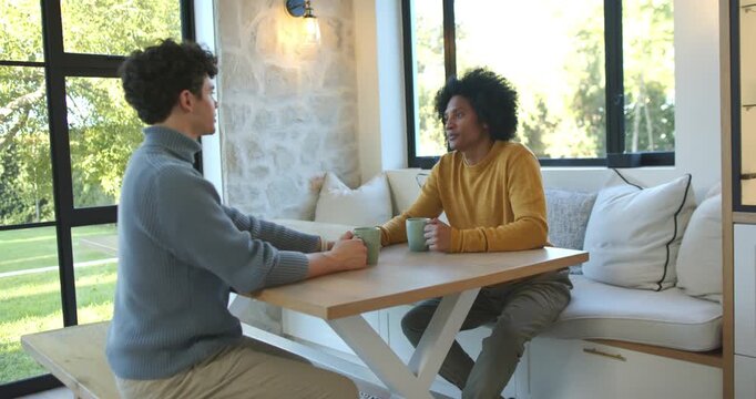Making eye contact, African American men sitting in nook, right chatting while holding green mugs