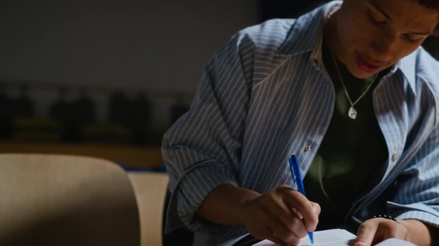 African American young adult student writing notes on theater script, camera tilting up. Footage suitable for arts education campaigns, drama academy marketing and creative storytelling projects